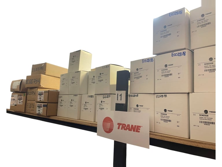 Stack of TRANE HVAC equipment and cardboard boxes on a black platform with company logo sign